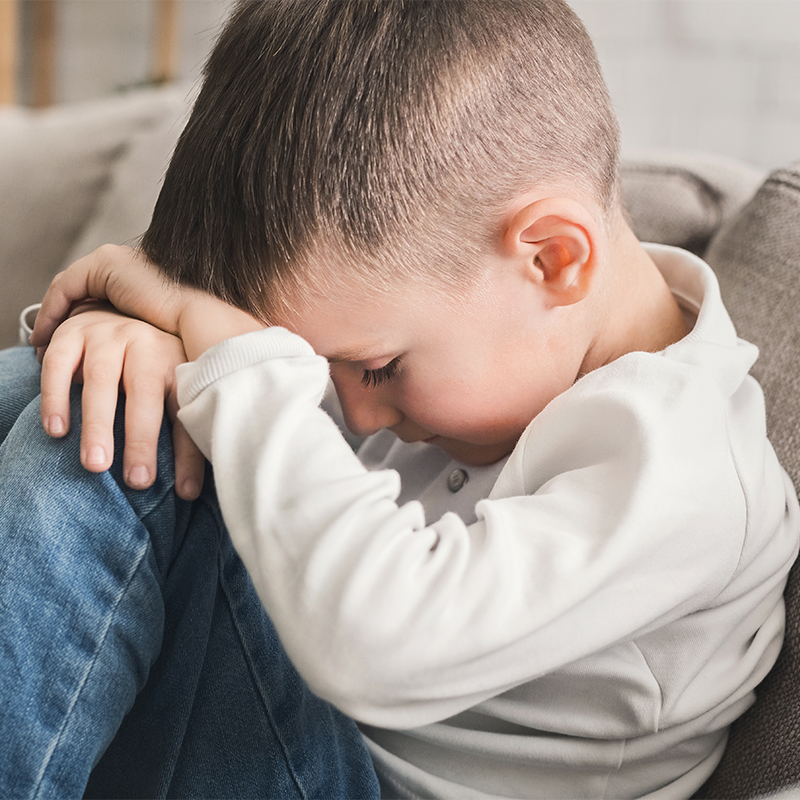 Crying child boy hugging his knees on sofa